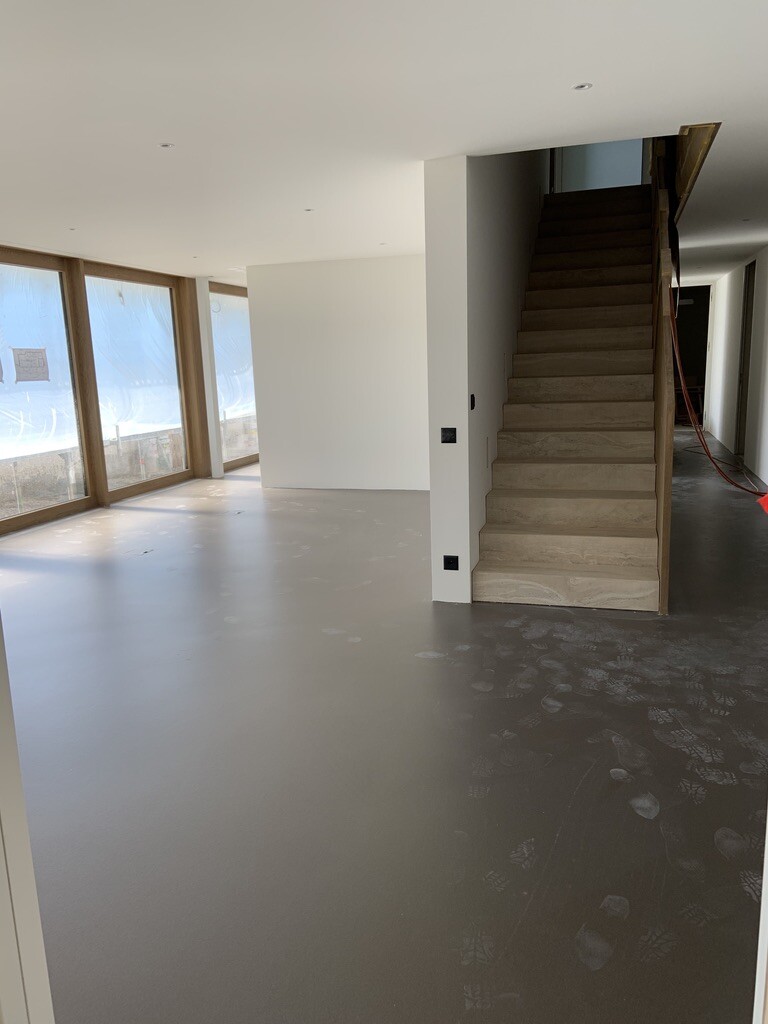 Open construction space with wooden stairs, large windows, and unfinished floor.