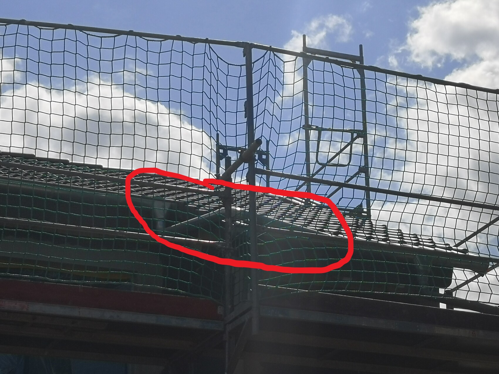 Safety net over scaffolding at a roof edge with tiles, blue sky in the background