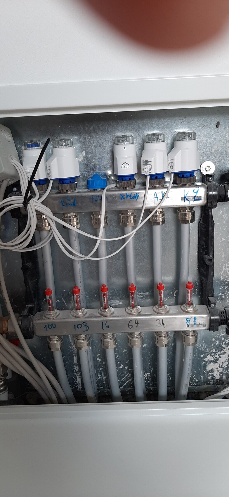 Heizungs-Verteiler mit sechs Rohren, roten Ventilgriffen, Kabeln und Beschriftung