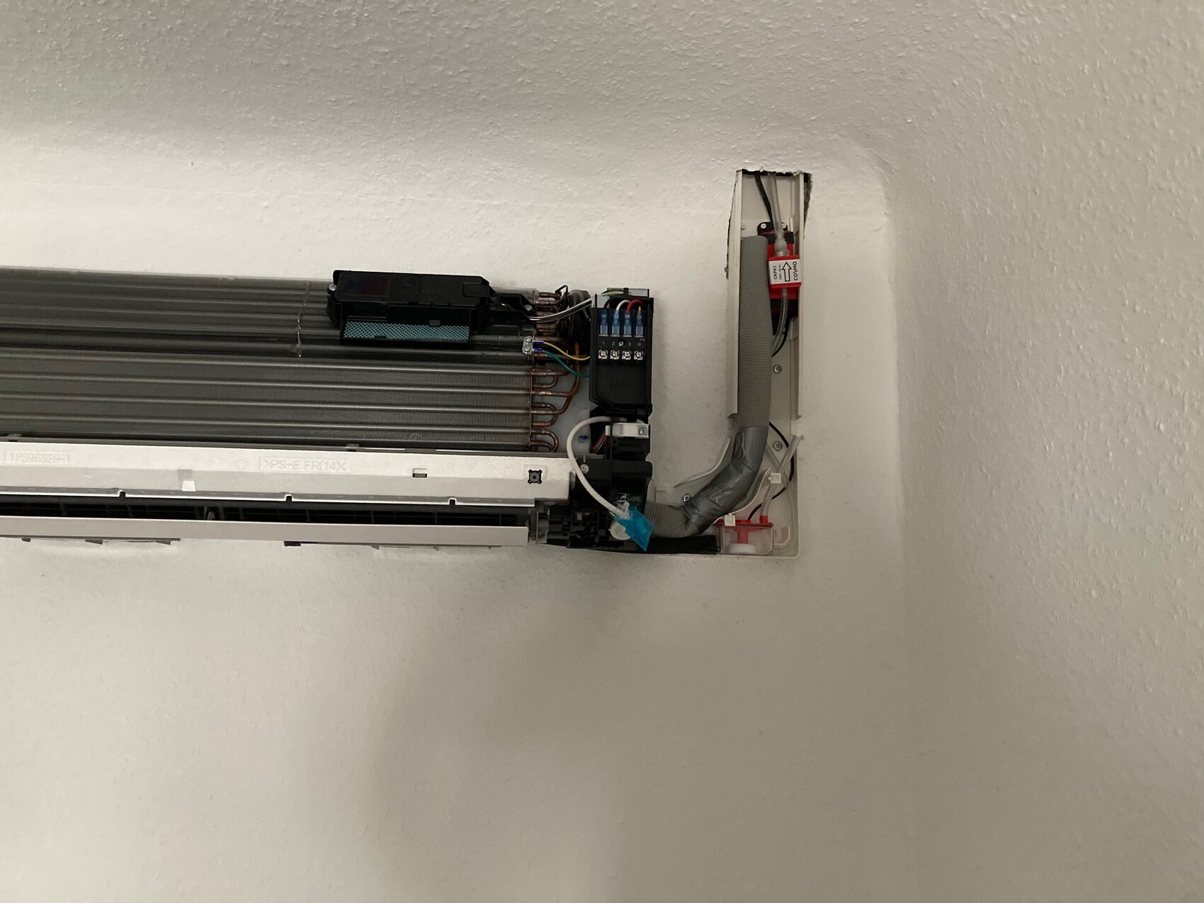 Open indoor unit of an air conditioning system with electronics, copper pipes, and cables on the wall.