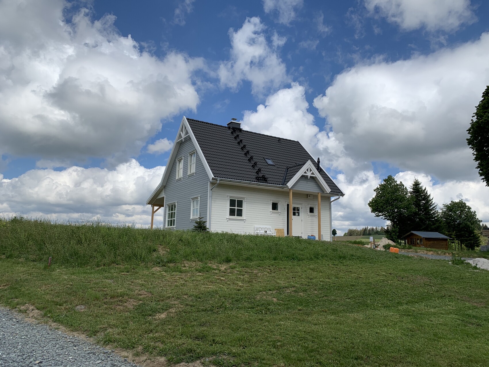 White single-family house with gray pitched roof on a green hill under a cloudy sky.
