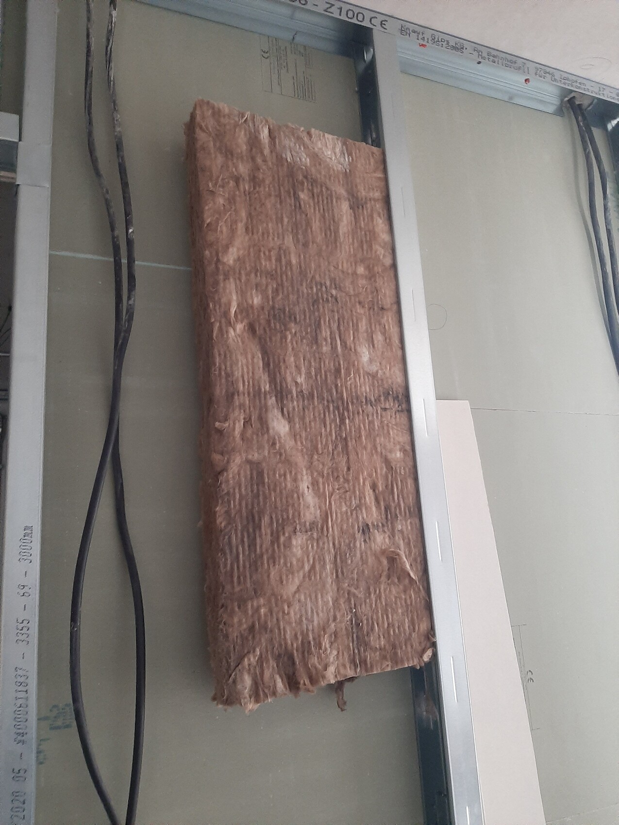 Brown wood wool insulation panel between metal studs, cables next to it.