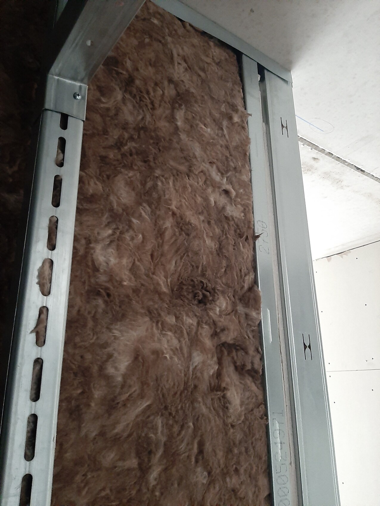 Wall cavity with brown insulation wool between metal framework and building elements.