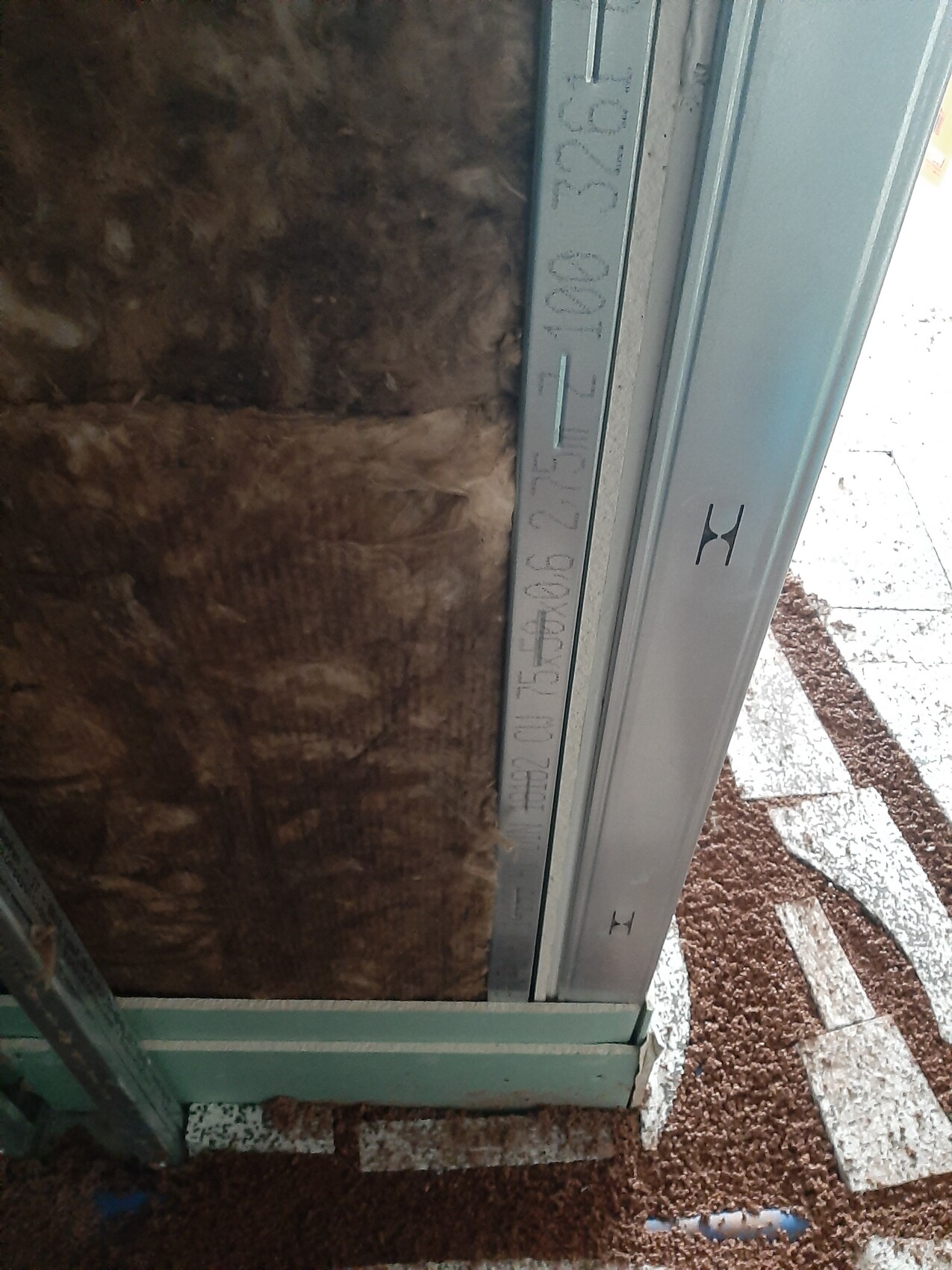 Close-up of a metal profile next to insulation, visible with measurement marks.
