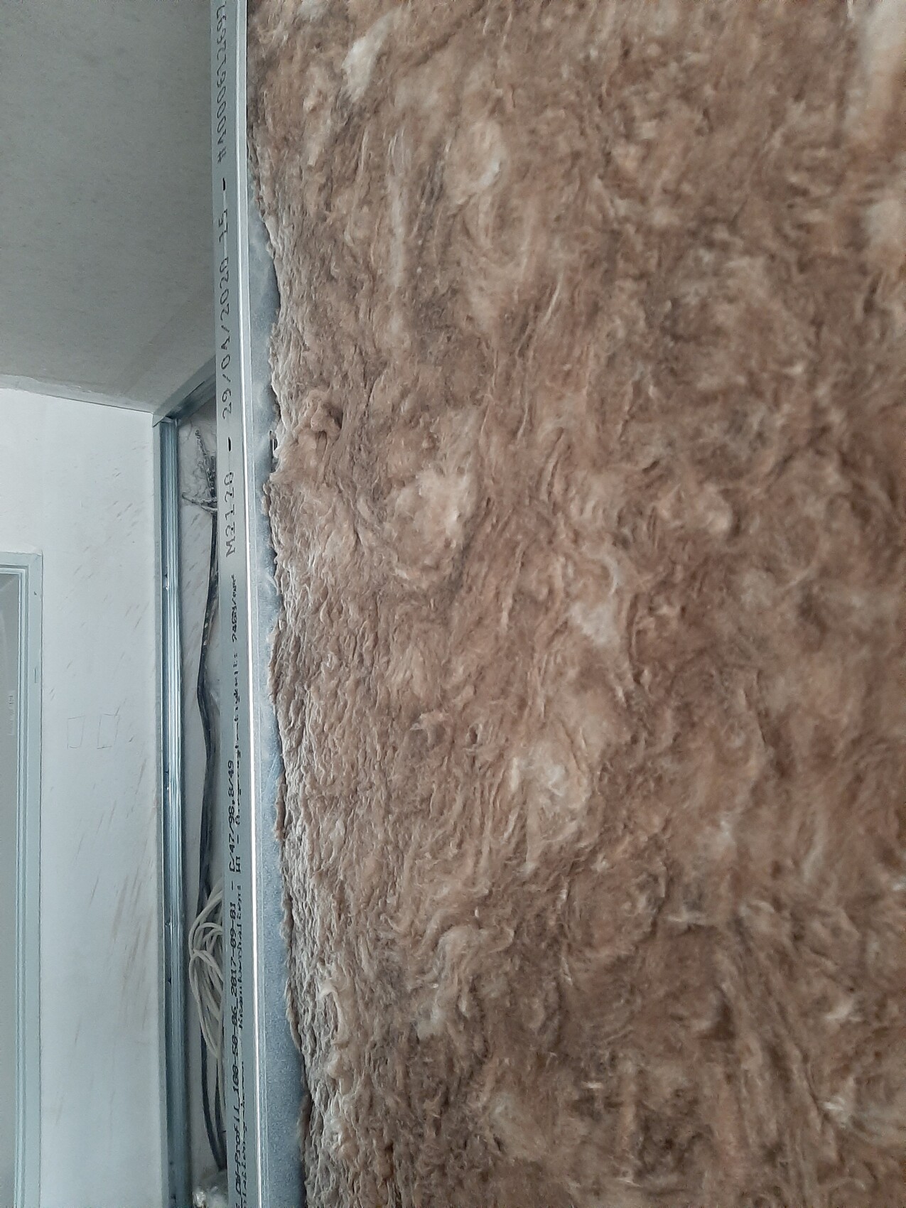 Brown insulation wool on wall next to metal frame, loose cables visible.