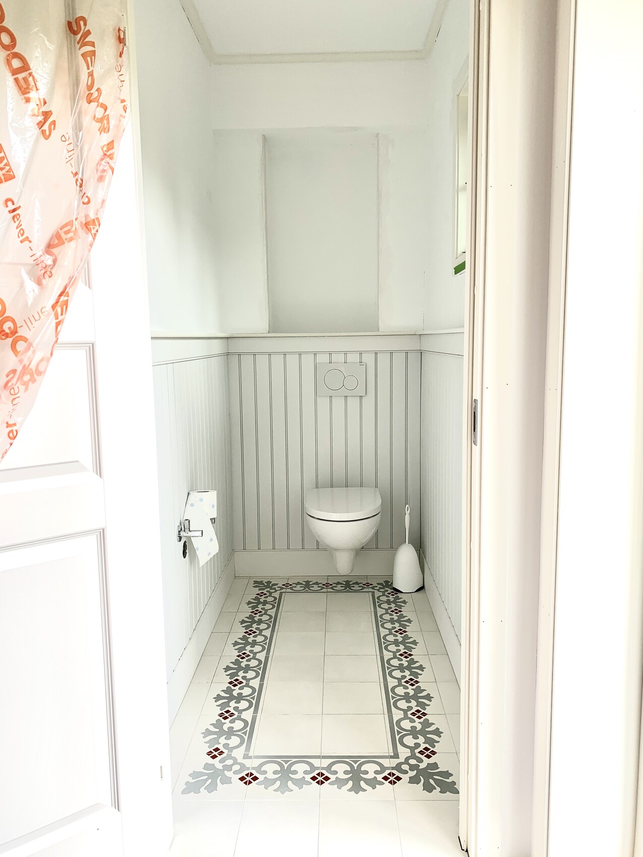 Bright guest bathroom with wall-hung toilet, toilet brush, and decorative tiled floor.