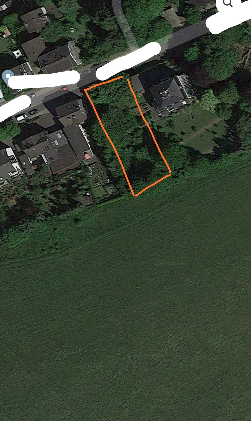 Satellite image of a residential neighborhood with a rectangular plot marked in orange next to a green area.