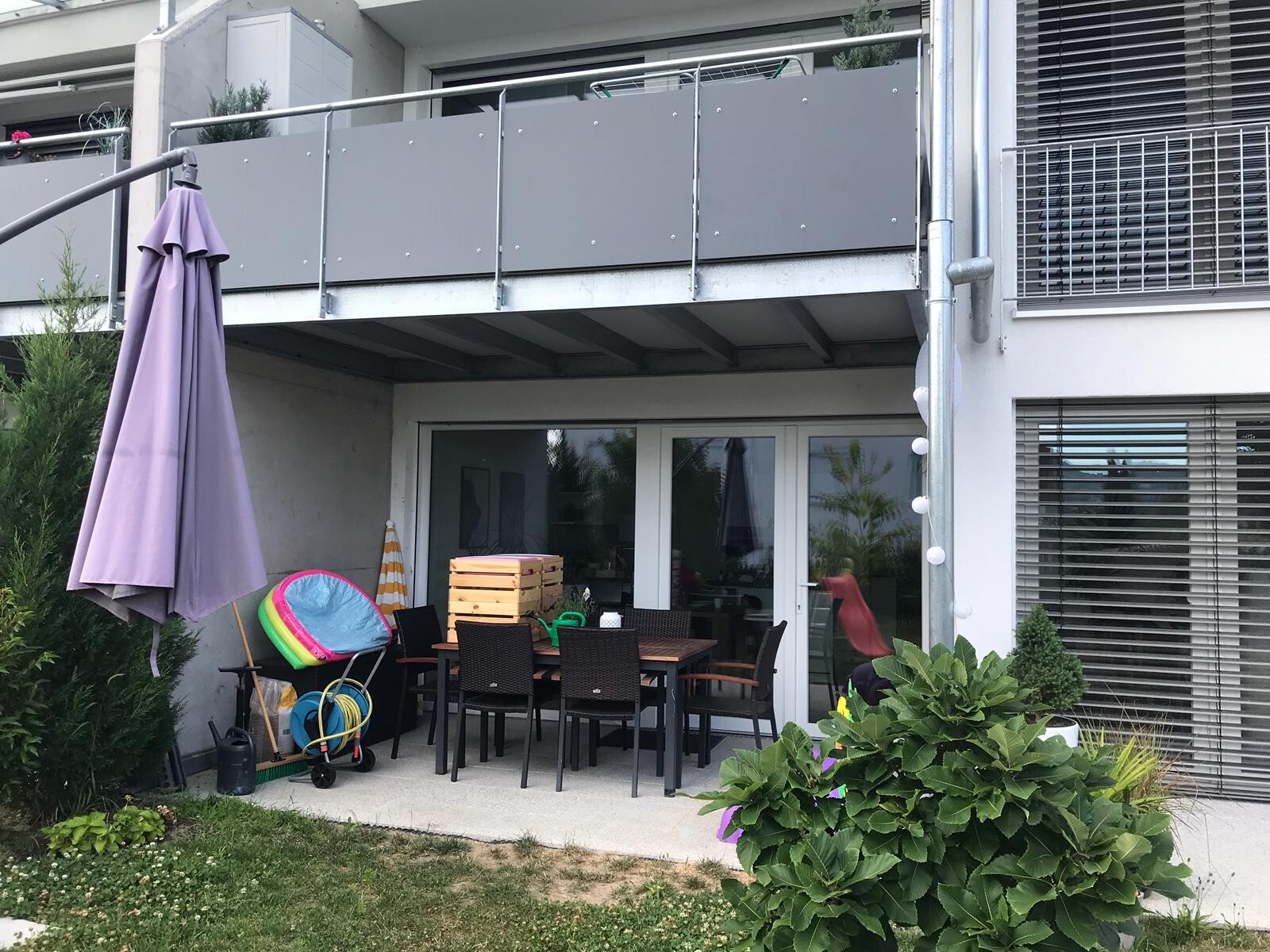 Apartment terrace with dining table, chairs, purple parasol, and wooden boxes