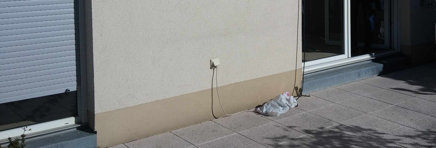 Outside wall of a house with socket, cables, and trash bag on terrace