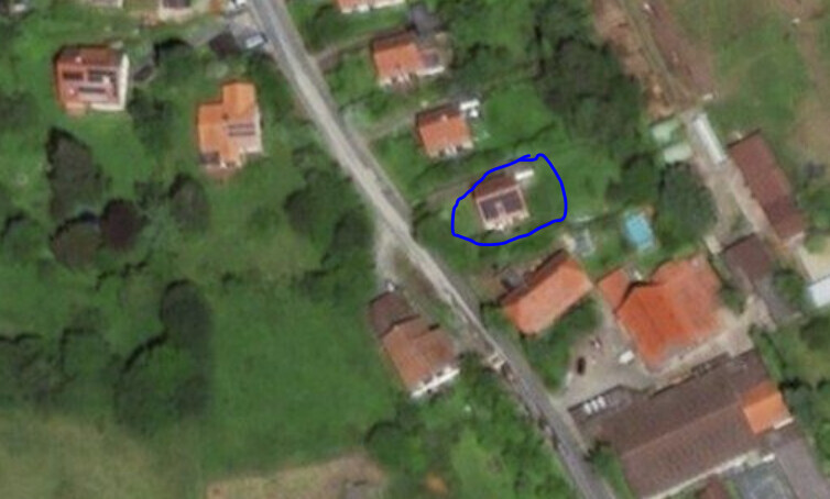 Aerial view of a village neighborhood with green areas; house marked in blue near the center.