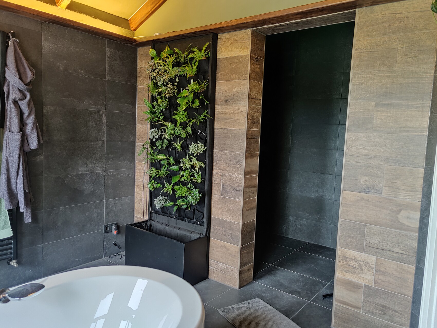 Modern bathroom with vertical plant wall, dark tiles, and a freestanding bathtub.