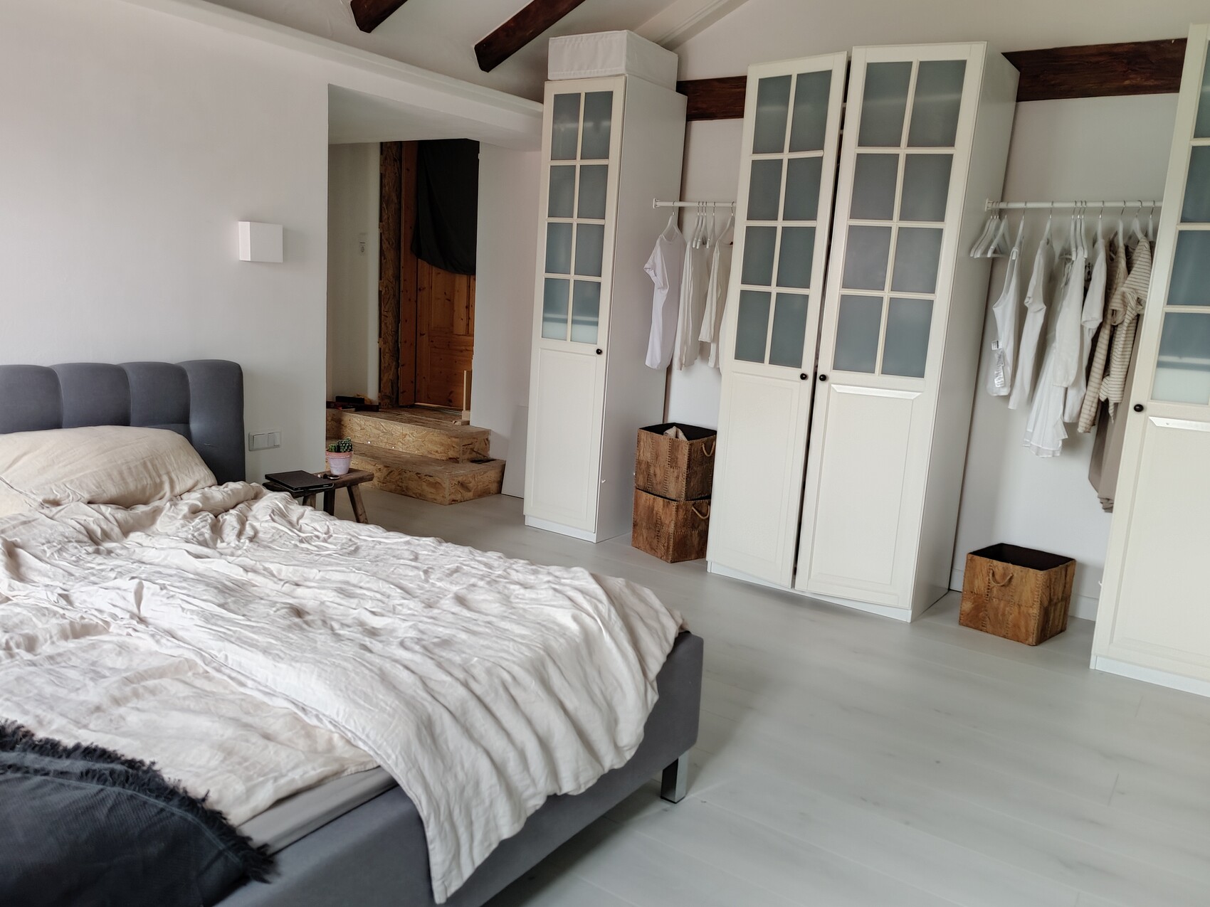 Bright bedroom with gray upholstered bed, beige ceiling, white wardrobes.