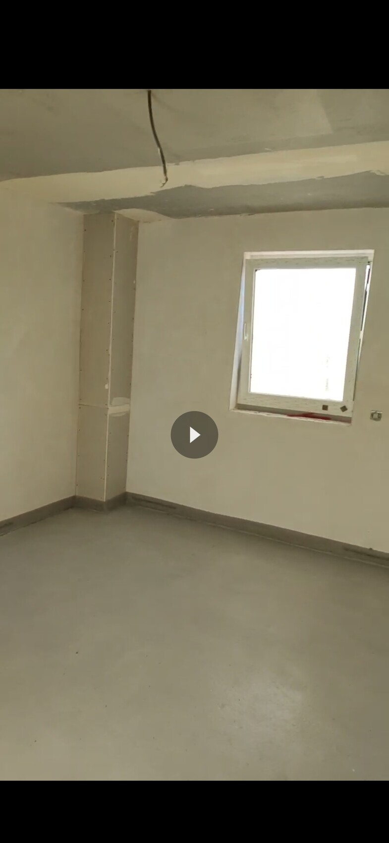 Empty, unfinished room with concrete floor, window on the right, loose cables hanging from the ceiling.