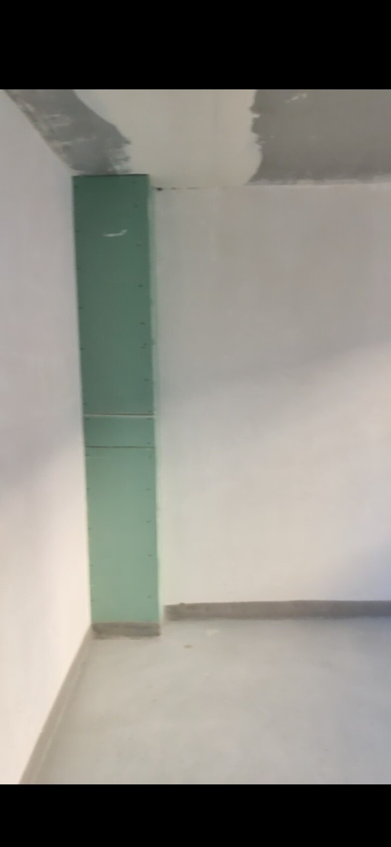 Empty room with green, vertical pillar-cabinet in the corner in front of a white wall.