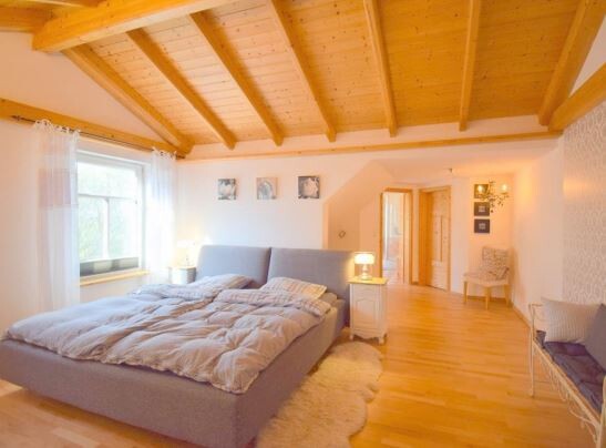 Bedroom with wooden beam ceiling, large bed, nightstands, lamps, and window.