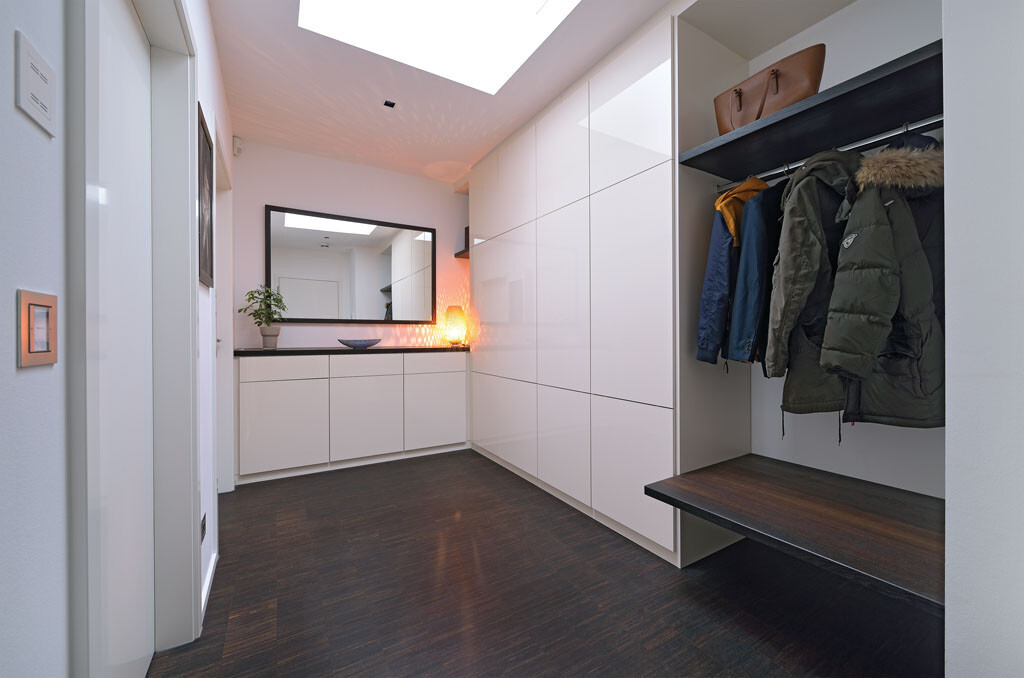 Modern hallway: white cabinets, wardrobe with coats, mirror, bench seat, and skylight.