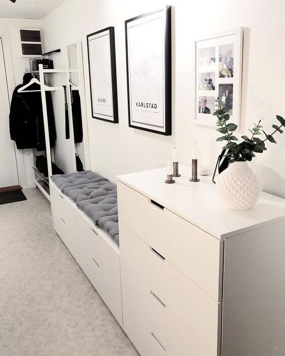 White hallway with wardrobe, upholstered bench, dresser, picture frame, and plant.