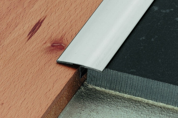 Close-up of a wooden panel with a silver cover strip over a black sealing membrane at the edge.
