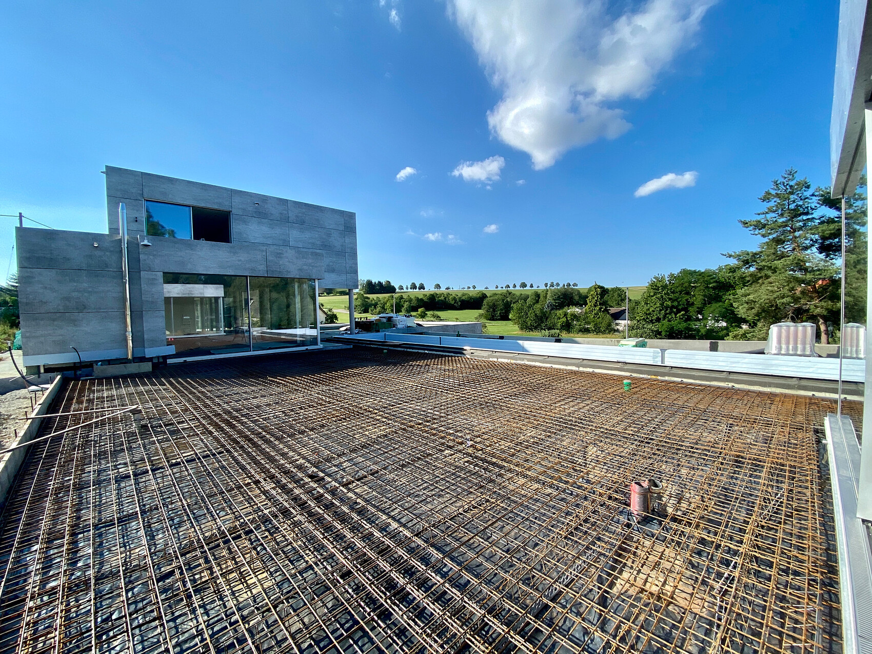 Modern building under construction; reinforcing steel on raw concrete floor, green landscape in the background.