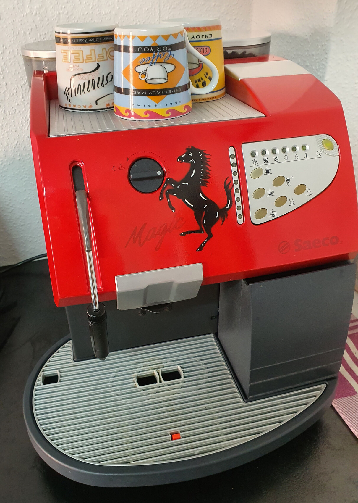 Red Saeco espresso machine with black horse motif and coffee cups on top