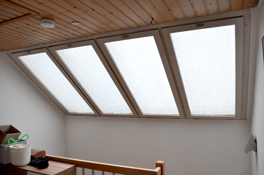 Interior with four slanted roof windows, wooden ceiling, railing, and items on the left.