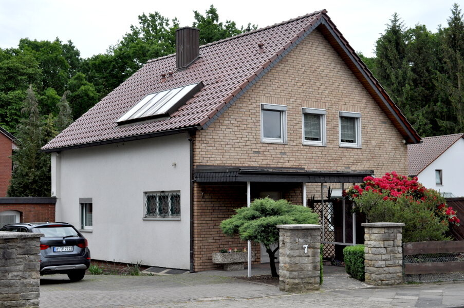Two-story detached house with red tile roof, solar panel, and front yard with tree.