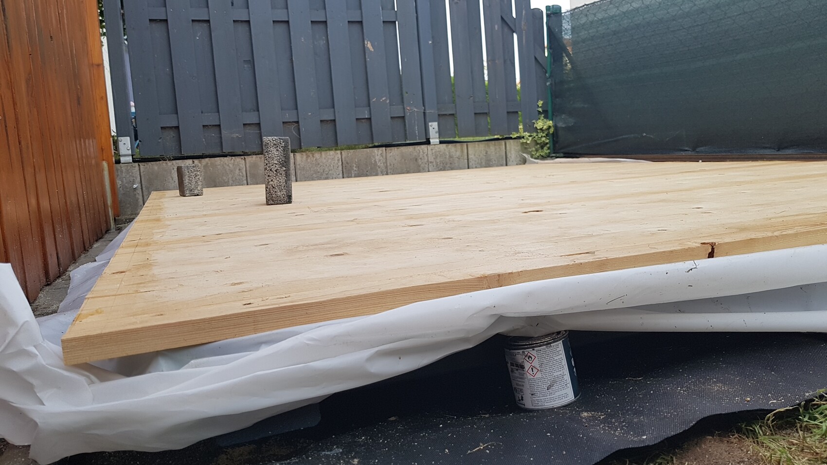 Temporary wooden platform in the garden, two concrete blocks on top, background fence and cover.