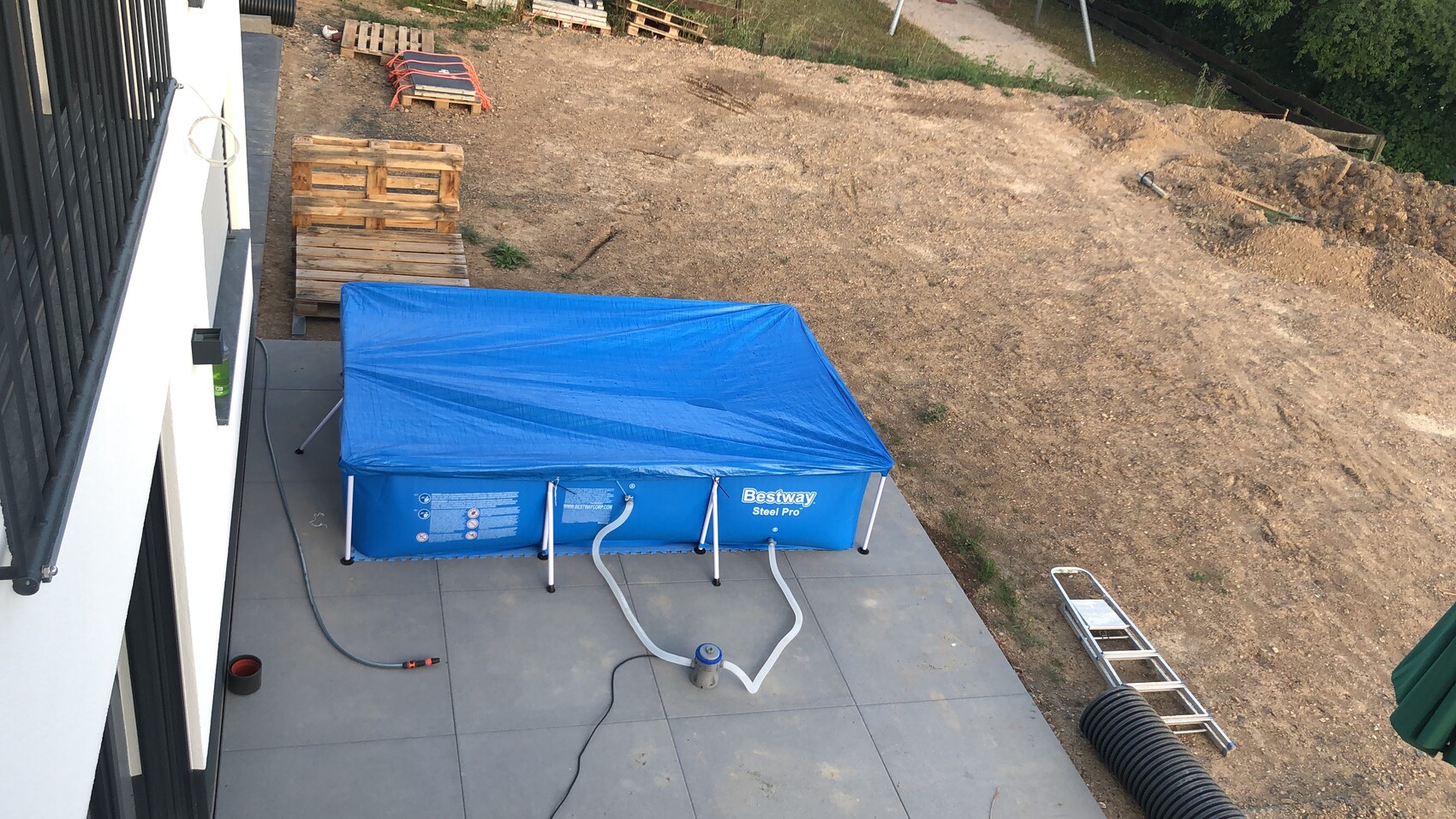 Outdoor area: Blue Bestway pool with cover, pump and hoses on terrace.