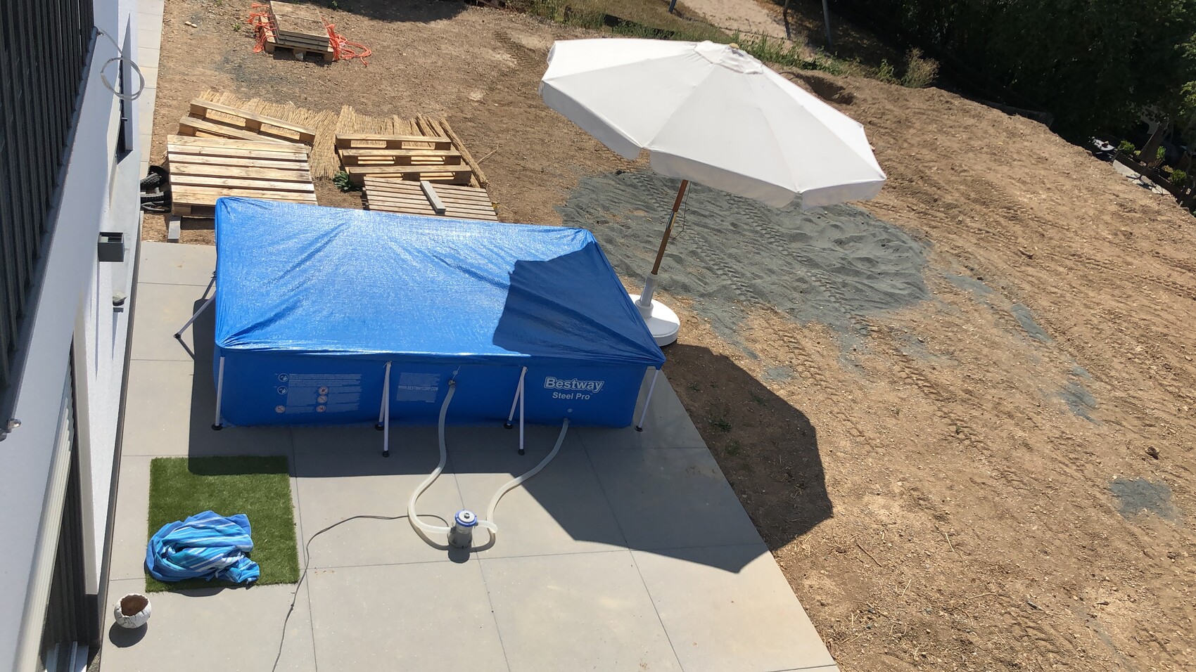 Landscaping construction site with blue Bestway Steel Pro pool, white parasol and pallets.