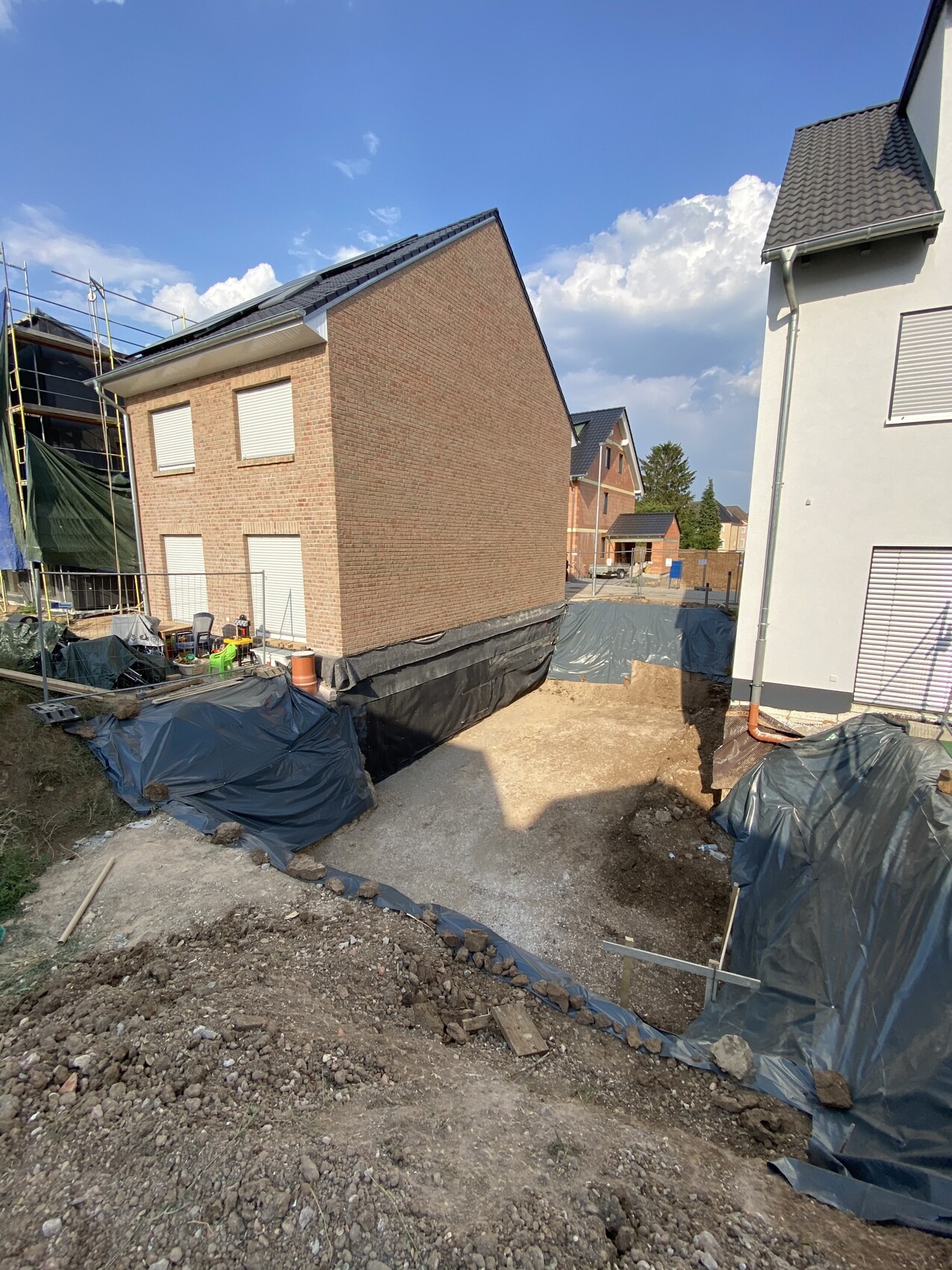 Construction pit between residential houses; tarps, soil, rubble, construction tools, blue sky
