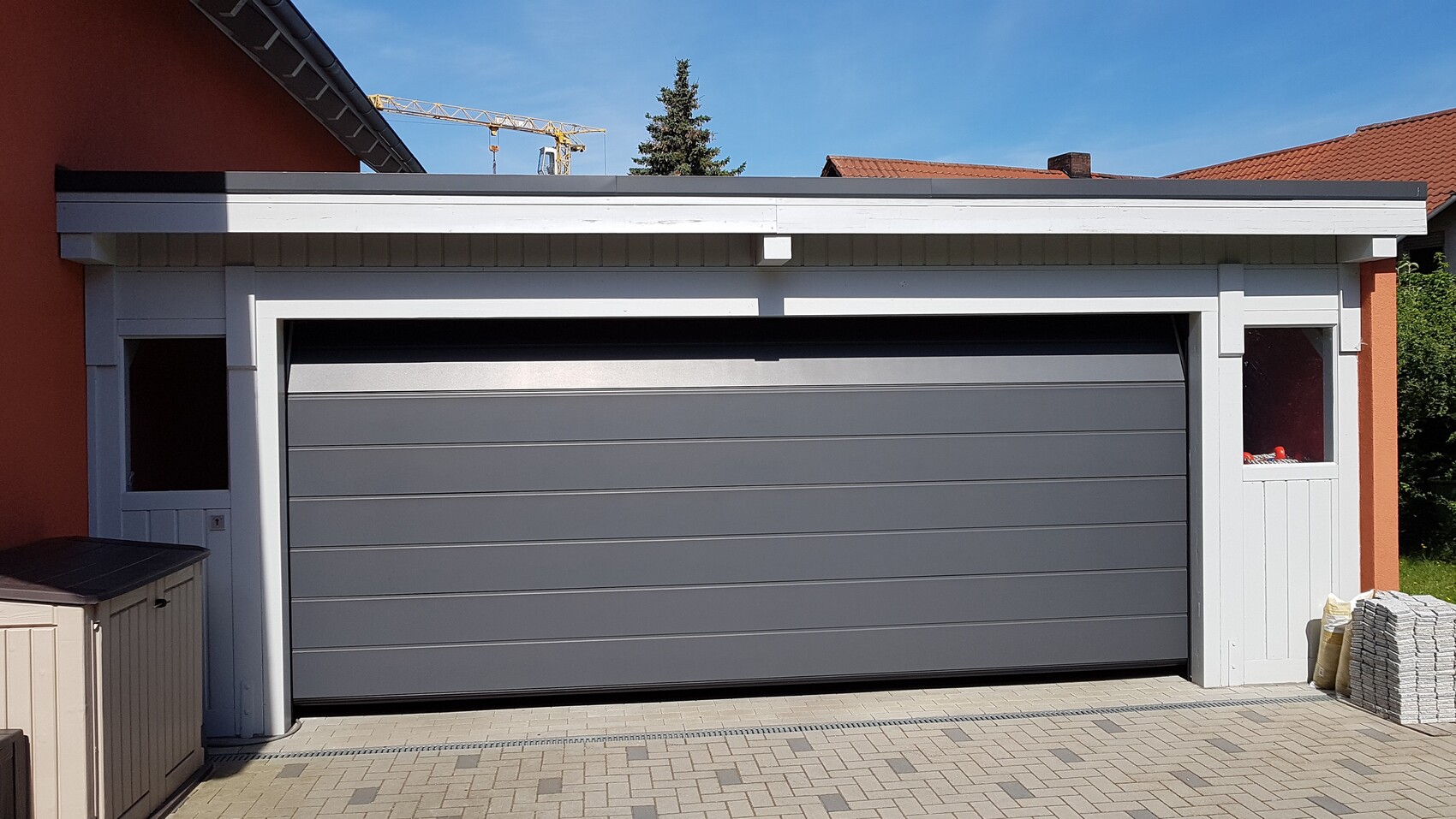 Garage with gray sectional door, white frame; orange wall on the left, paving stones on the right.