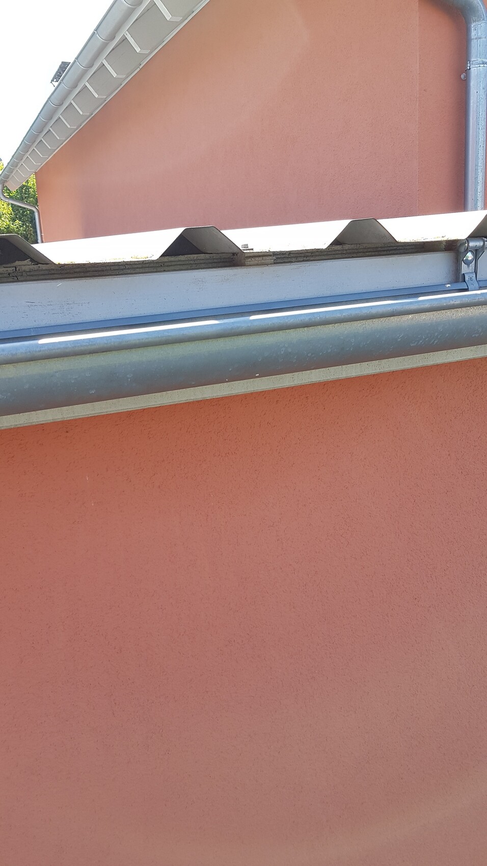 Pink plastered house wall with gutter, downpipe, and roof edge