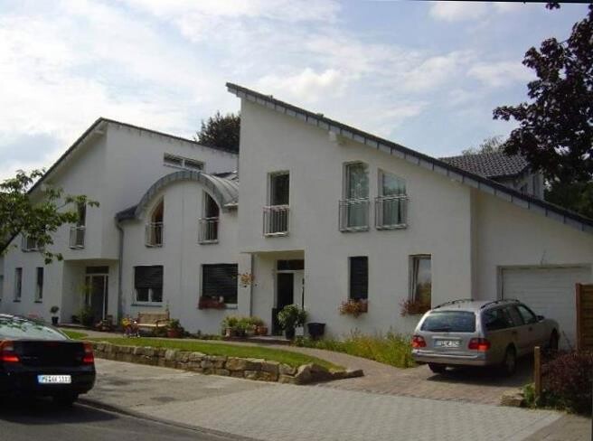 White residential facade with large windows, driveway and parked cars