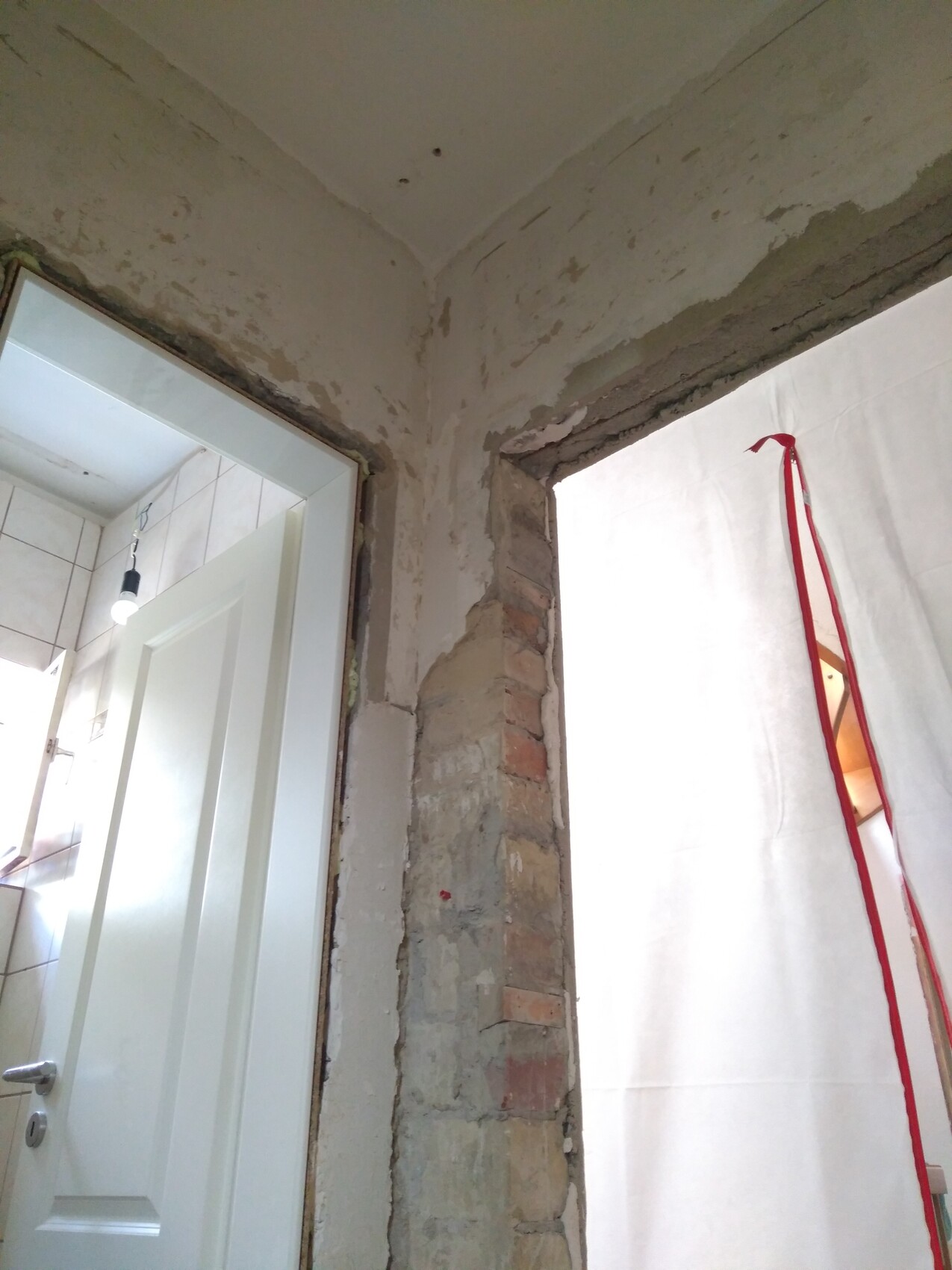Room under renovation with exposed masonry, open door frame on the left, white sheet on the right.