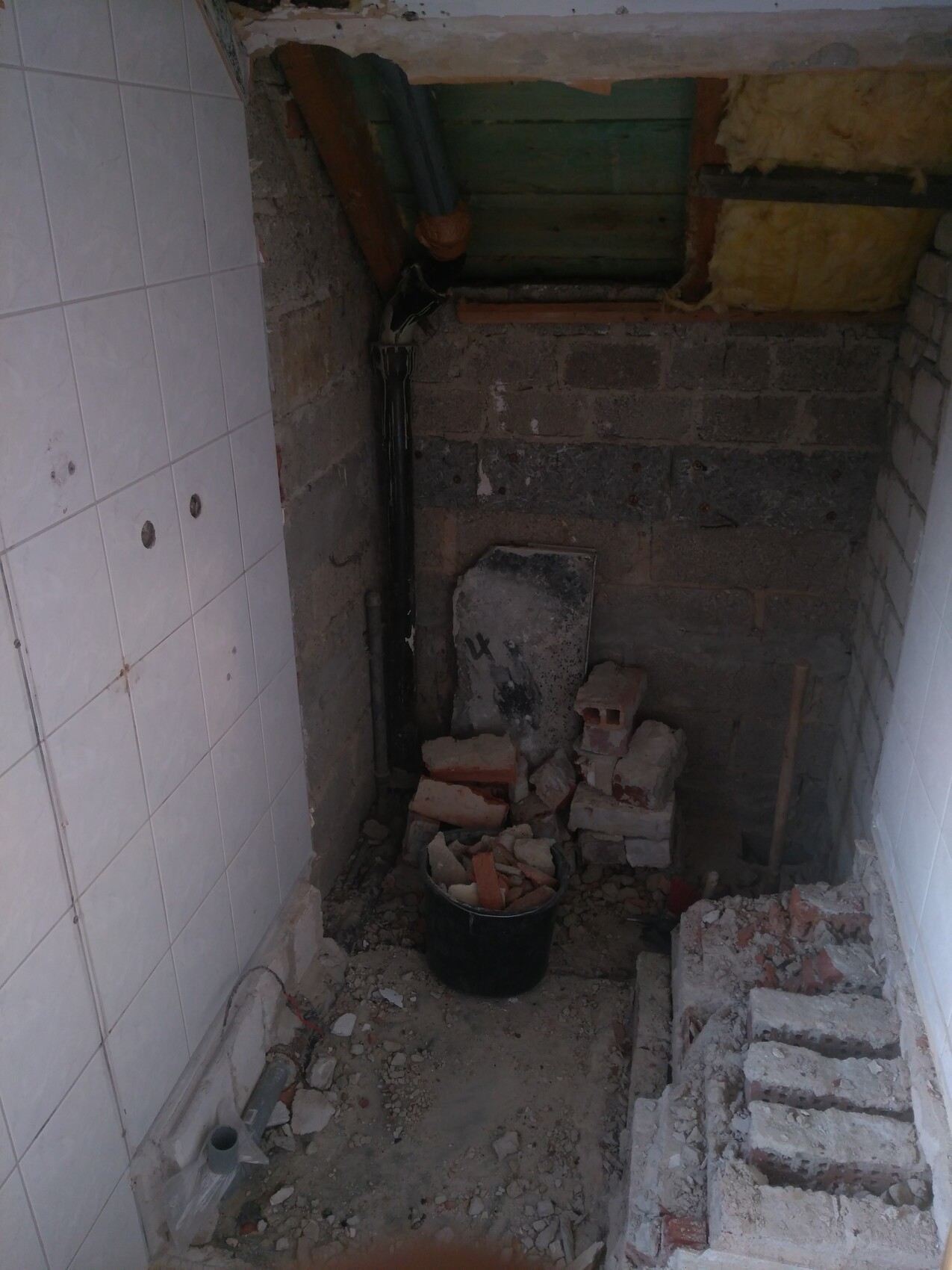 Tight construction area: brick debris, concrete blocks, black pipe, bucket with rubble, structural walls.