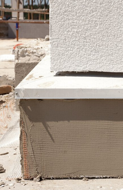 Close-up of a shell construction: concrete block on foam foundation, scaffolding in the background.