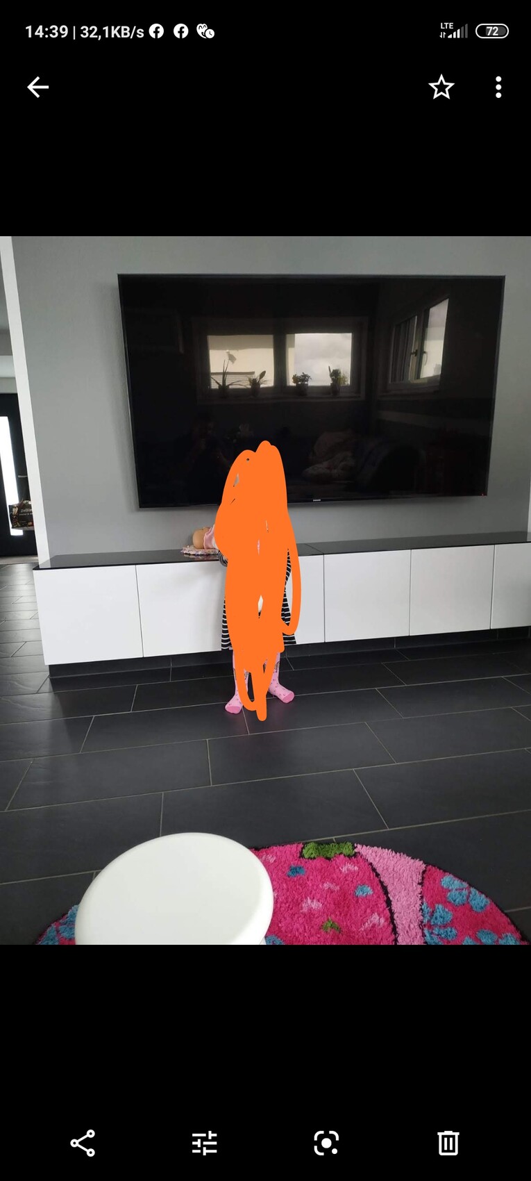 Large flat-screen TV in the living room in front of white lowboard and dark floor tiles