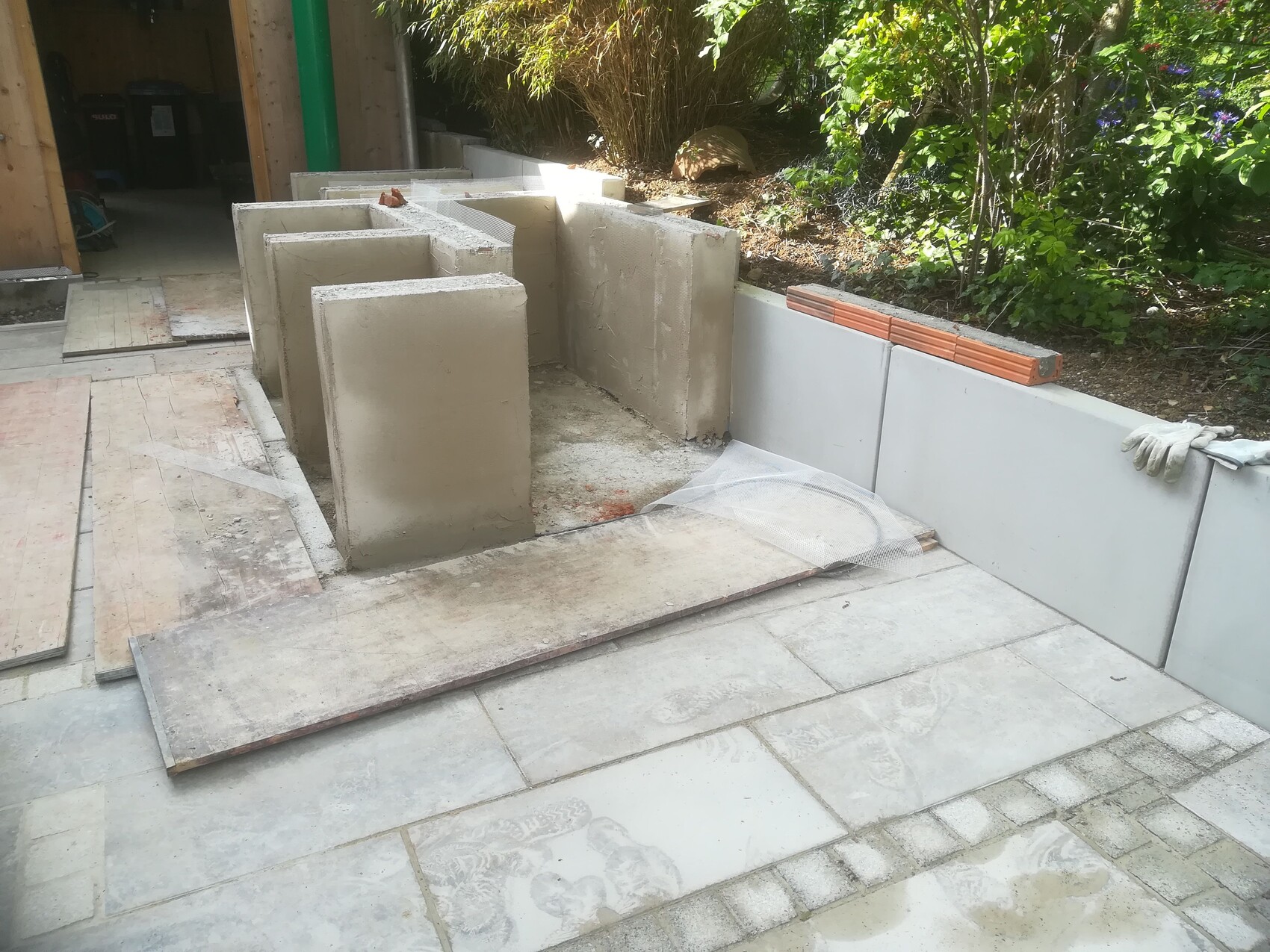 Garden construction site: concrete blocks forming a wall, wooden boards lying next to it, gloves on the edge.