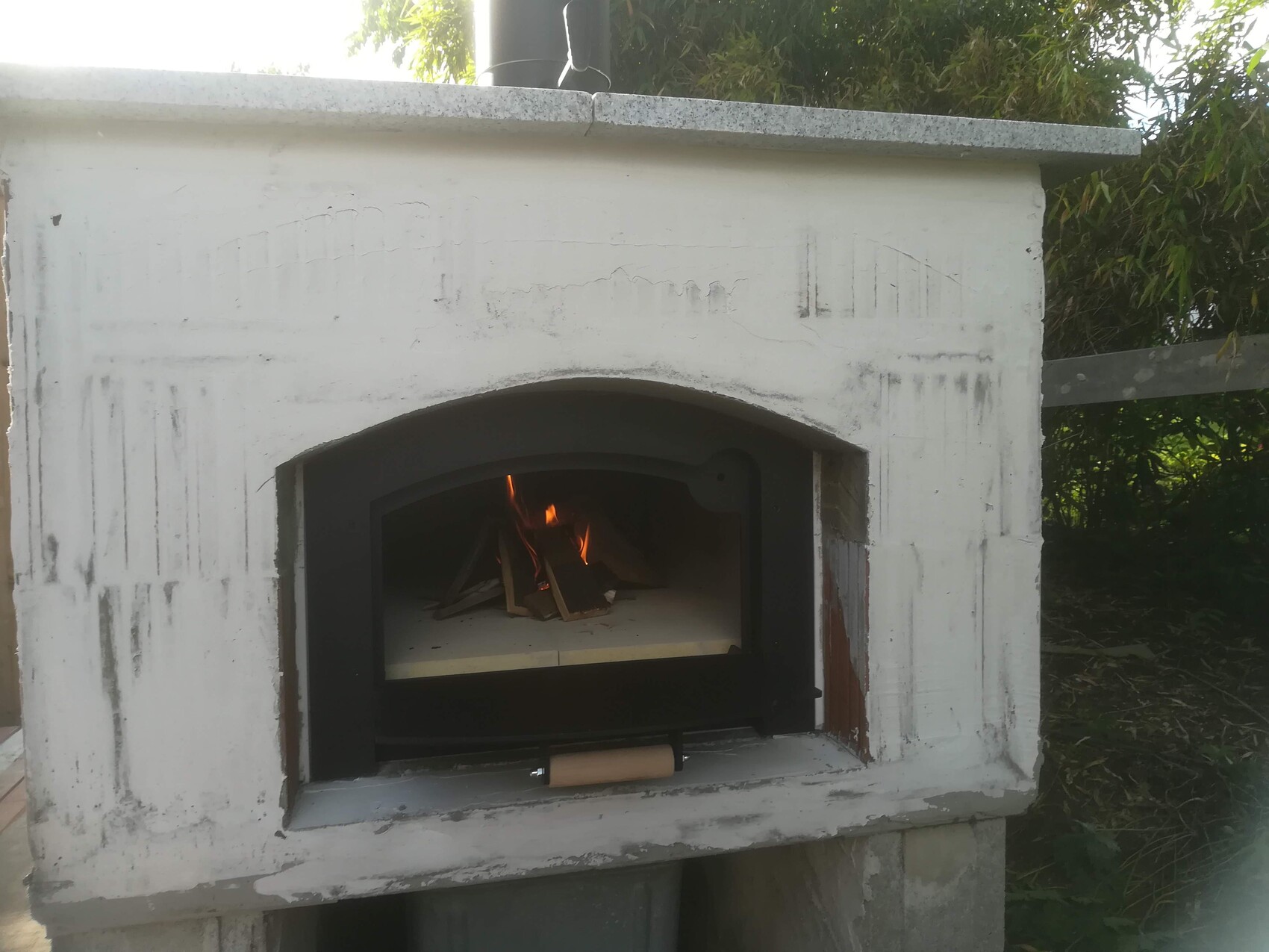 Outdoor baking oven made of concrete, open fire chamber with burning wood fire.