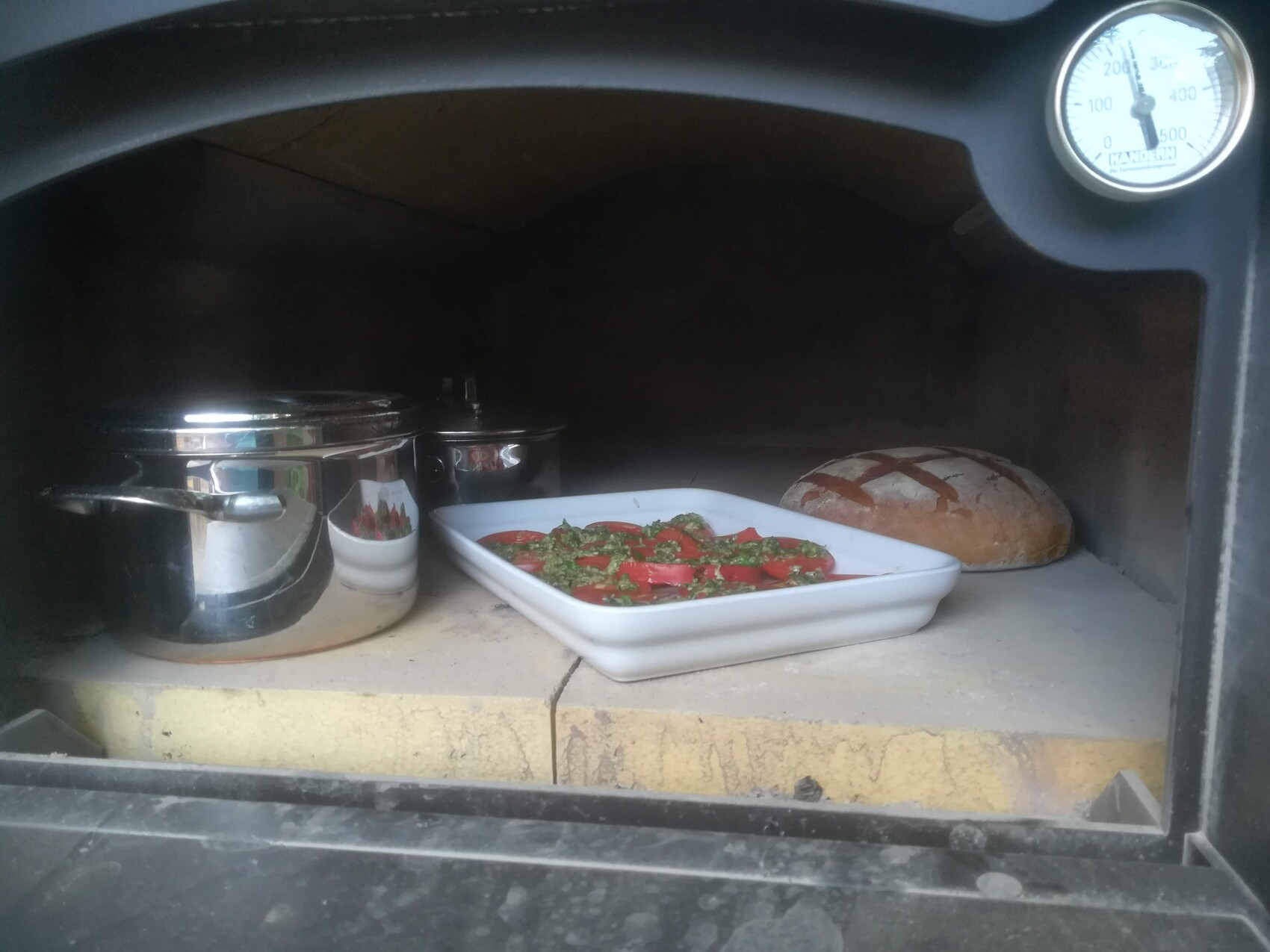 In the oven: white casserole dish with red tomato vegetables and herbs; bread next to it.