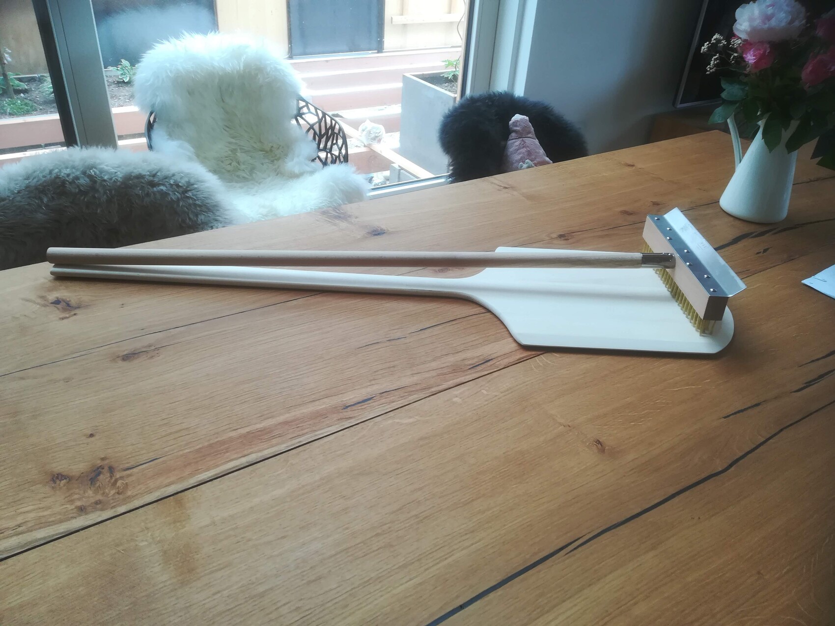 White cleaning tool with brush head lying on wooden table; next to it two metal rods.