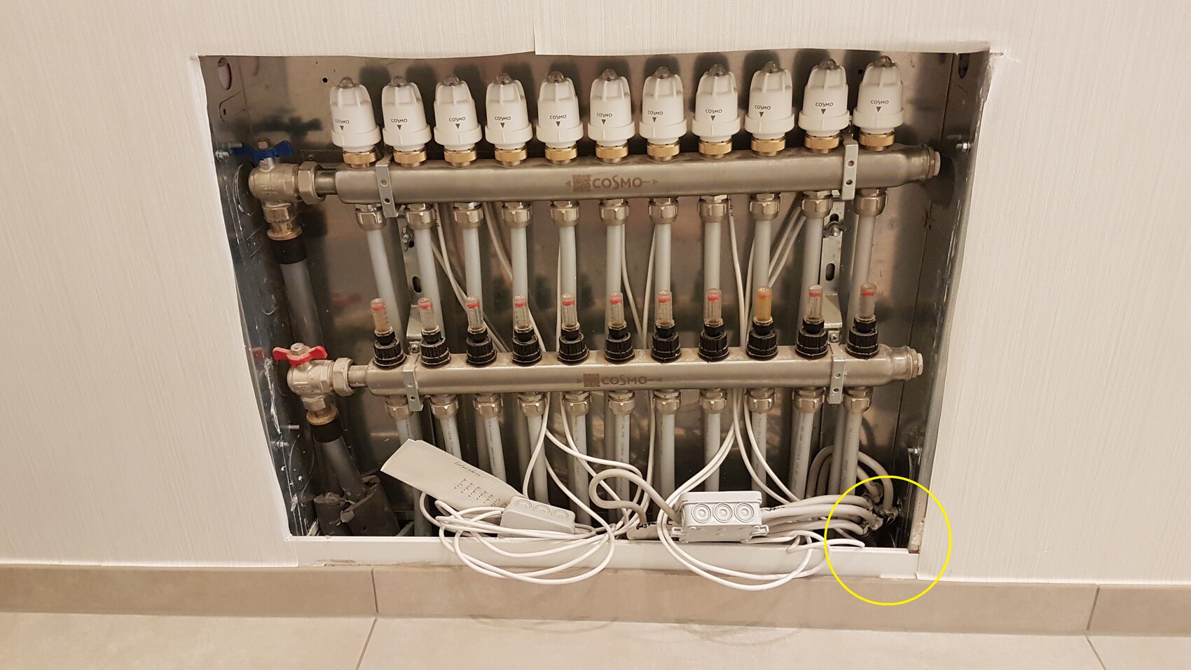 Heizkreisverteiler mit vielen Rohren, Ventilen und Kabeln in Wandnische; unten Kabel am Boden.