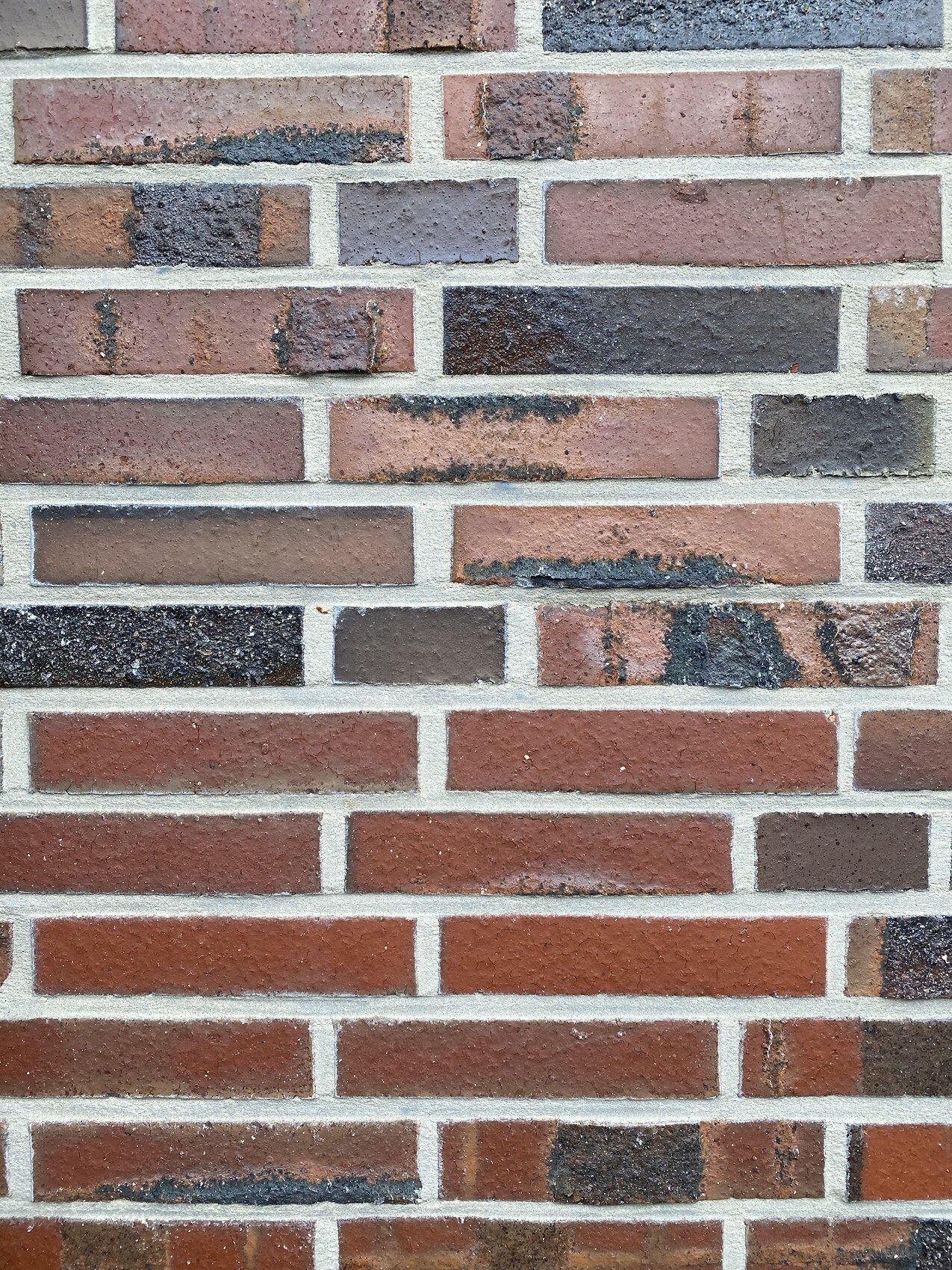 Brick wall made of red and brown bricks with gray mortar.
