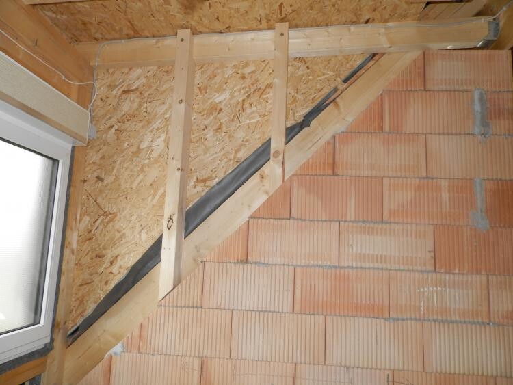 Construction site: timber frame, OSB cladding, diagonal stair structure, brick wall on the right.