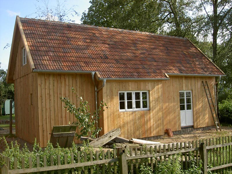 Small wooden house with red tiled roof, white window, door, ladder and wooden fence in the foreground