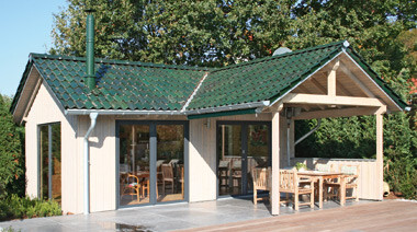 Small wooden house with terrace in front of forest, green tiled roof