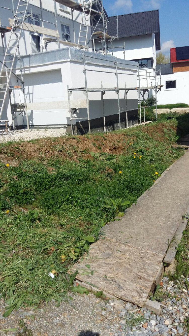 Multi-storey house with scaffolding, white facade; grassy area and wooden plank path in front.