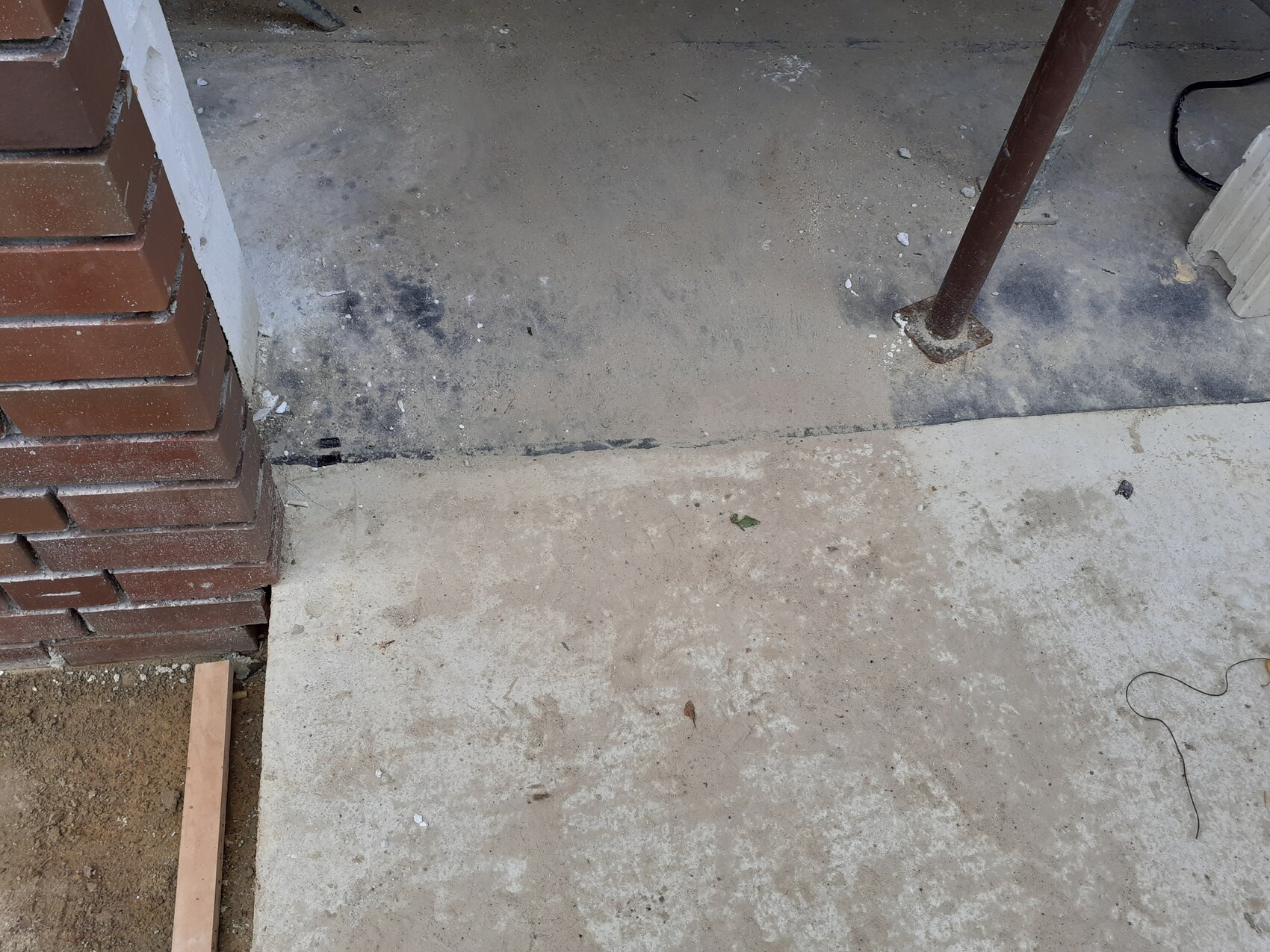 Baustellenszene: Betonboden, linke Ziegelwand, rostiges Rohr und Kabelreste.