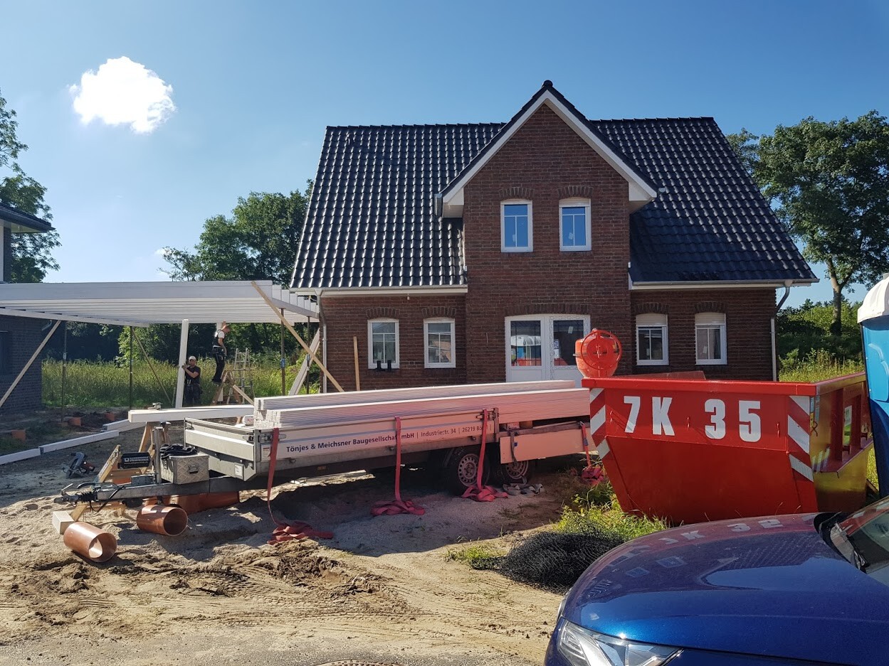 Rotes Backsteinhaus im Bau mit Bauholz, Geräten und einer Mulde davor.