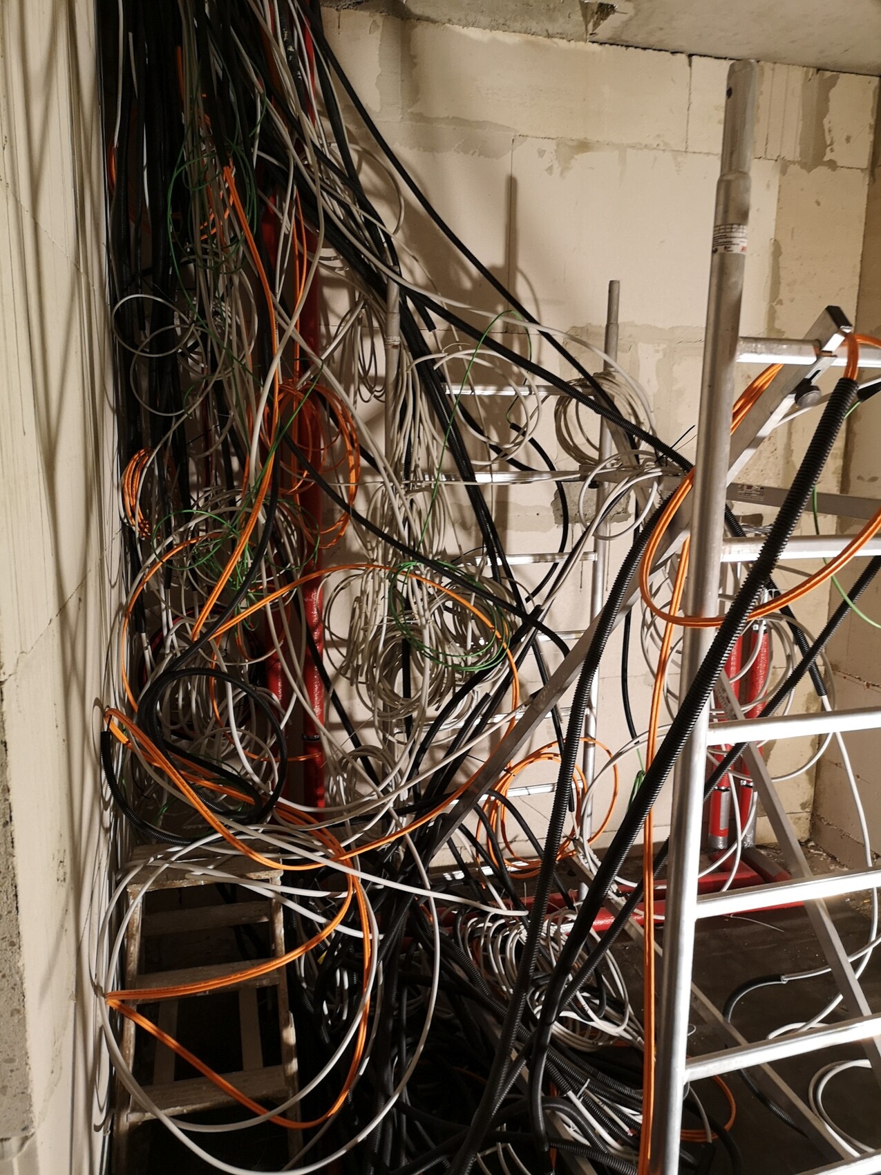 Entangled cables in construction/technical room; orange, black and white, swirling around a ladder.